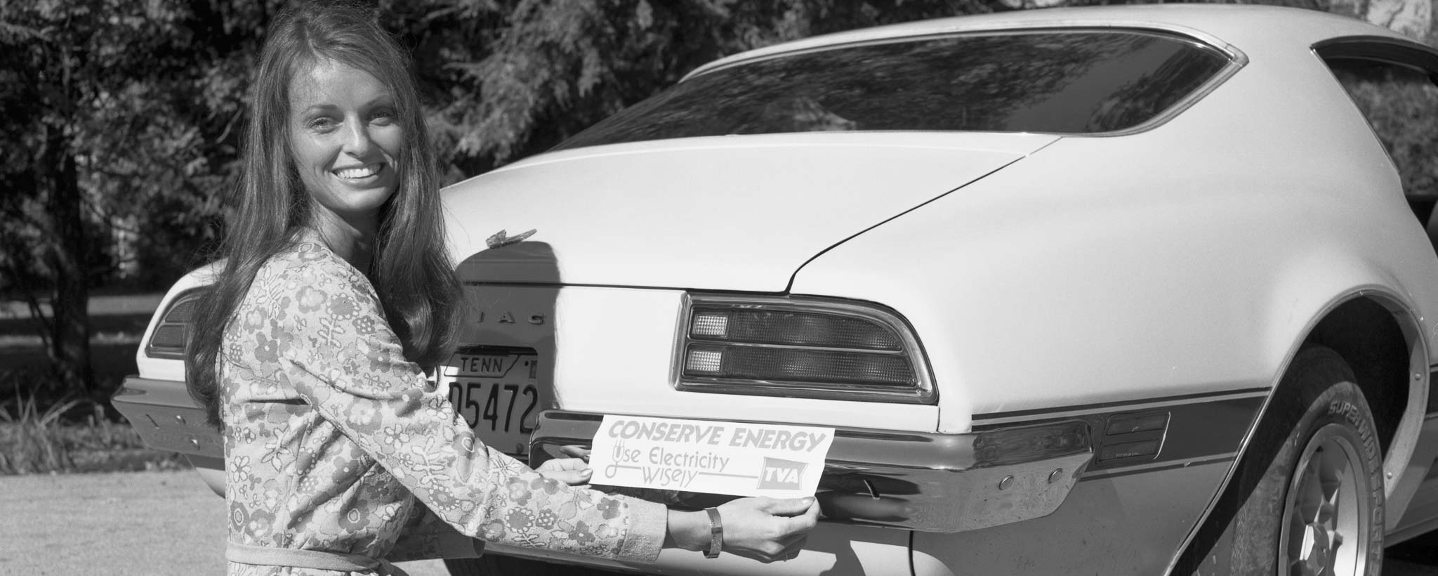 1970-hero-73186 woman putting on a "Conserve Energy" bumper sticker