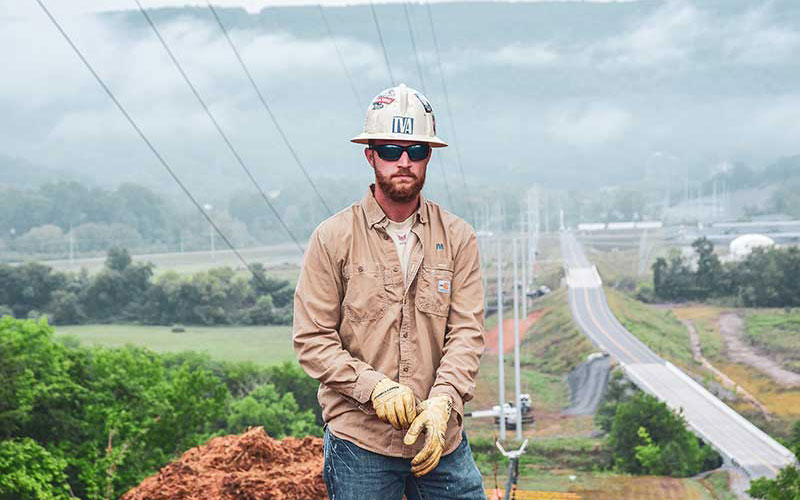 Lineworker stands on hill with power lines stretching into the valley
