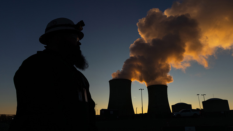 Silhouette of employee against a dark sky with cooling towers in the background