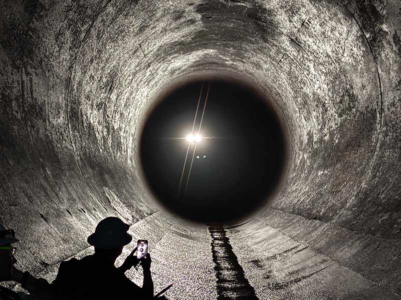 Crew members silhouetted against the drone’s light as it flies through the penstock.