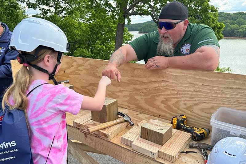 Student fist-bumps a TVA carpenter after successfully driving a nail into a block of wood.