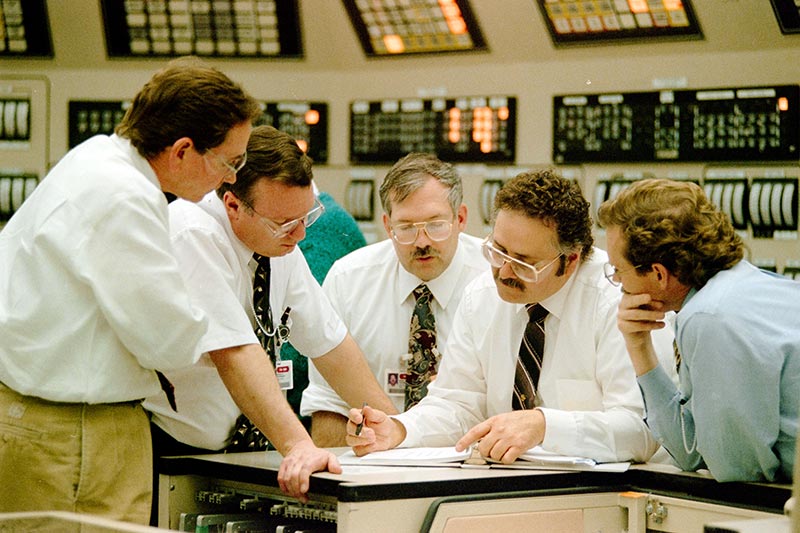 In this 1996 main control room photo, an industry observer, far left, looks on as (left to right) operations manager Terry Stockdale, reactor engineers Rory Warren and Tom Huth, and plant manager Rick Purcell plan for Unit 1 commercial operation.