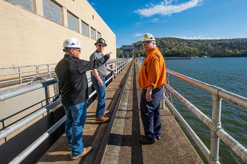 Adams point to boats off in the distance as Porter and Miller chat with him at Guntersville Dam.