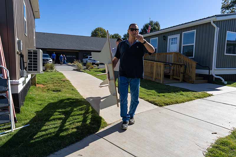 Volunteers carry a bed past a tiny home