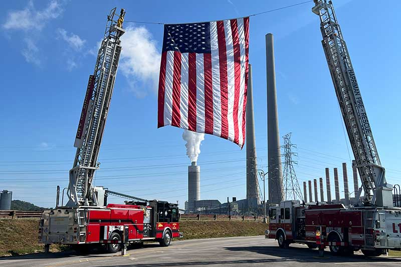 An American flag was suspended by two ladder trucks with the Kingston Fossil Plant in the background.