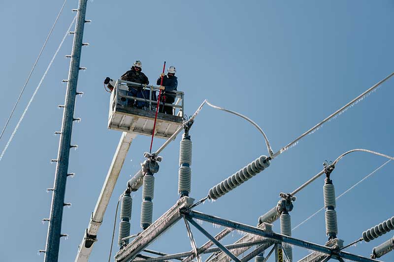 TVA lineworkers in bucket lift above powerlines covered in ice