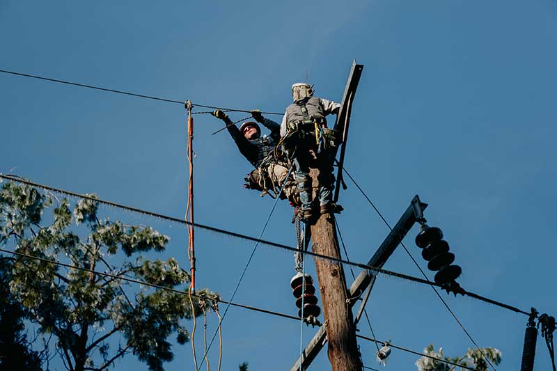 Lineworkers work from pole to connect broken lines