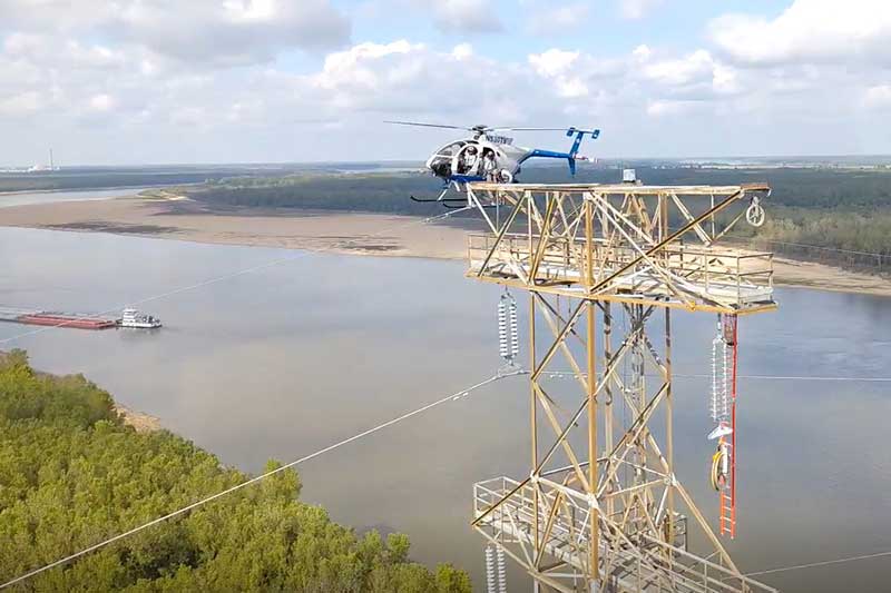 Helicopter hovers near transmission tower to help install wire