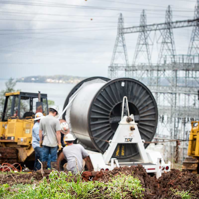 Lineworkers with large spool of wire with transmission towers in the background