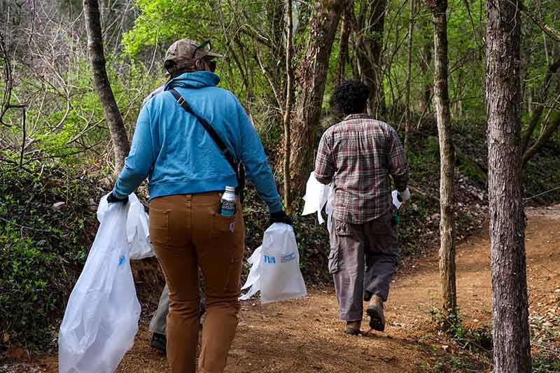 Volunteers walking along trail holding trash bags
