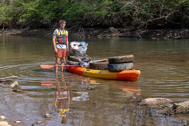 Man with kayak in water loaded with tires and other trash