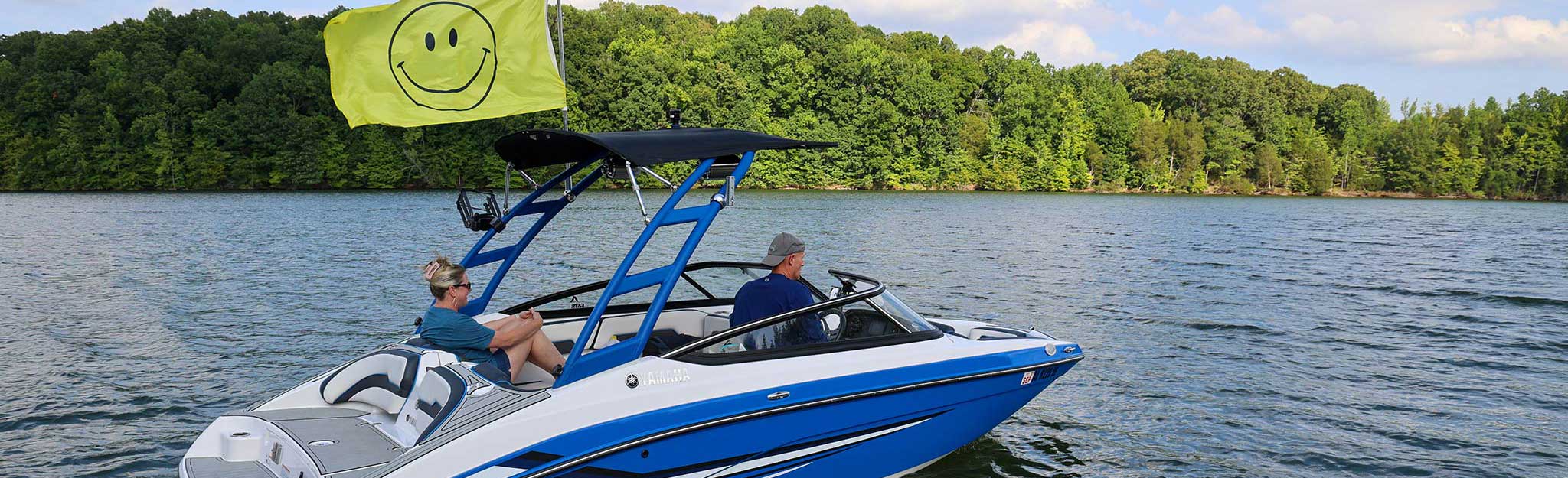 Boaters drive across a reservoir with a smiling face flag flying from the boat.
