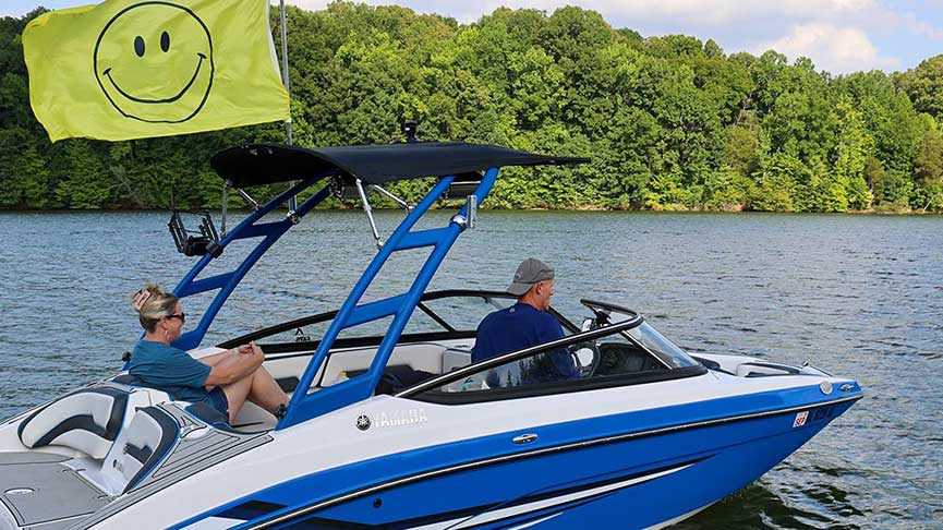Boaters drive across a reservoir with a smiling face flag flying from the watercraft
