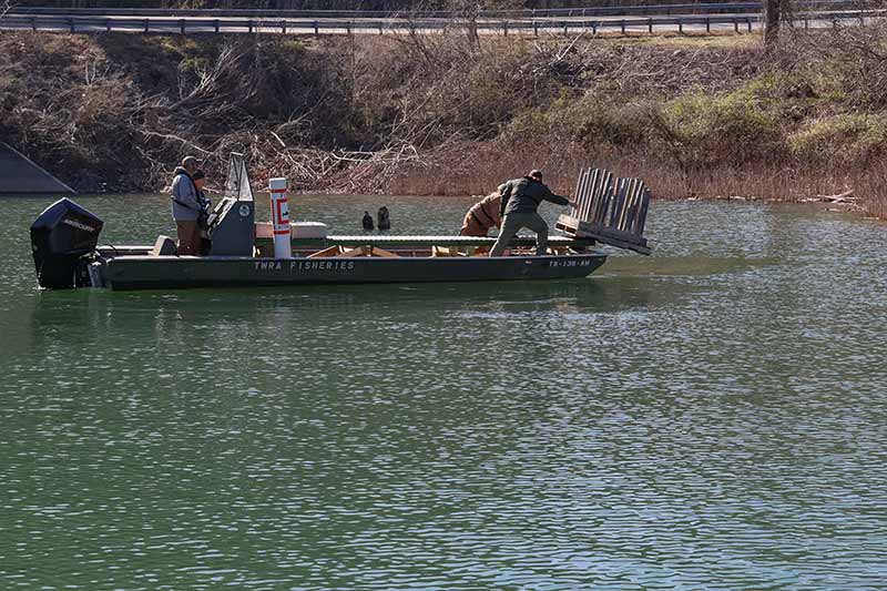 Men on boat pushing fish habitat structure into lake