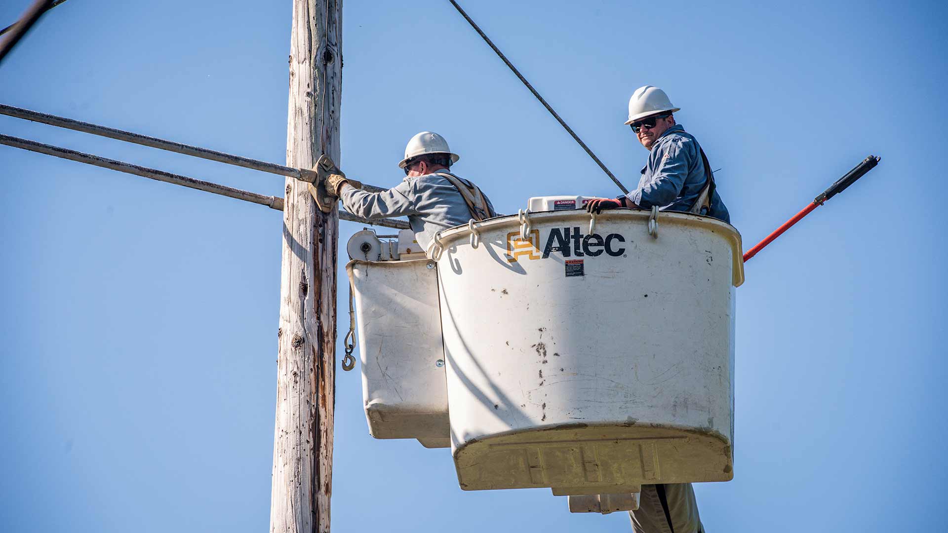 Jimmy Hinch and Josh Hinch remove hardware from a wood utility pole.