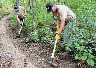 Two TVA team members use digging implements to clear a trail’s edge at Loyston Point during the National Public Lands Day activities