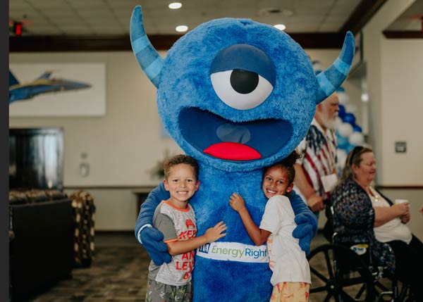 Two children hugging a blue one-eyed mascot with
