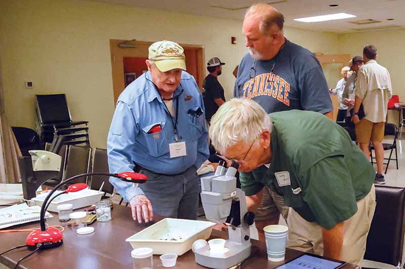 Clayton Gist, Dennis Baxter and Larry Ward take turns looking through microscope.