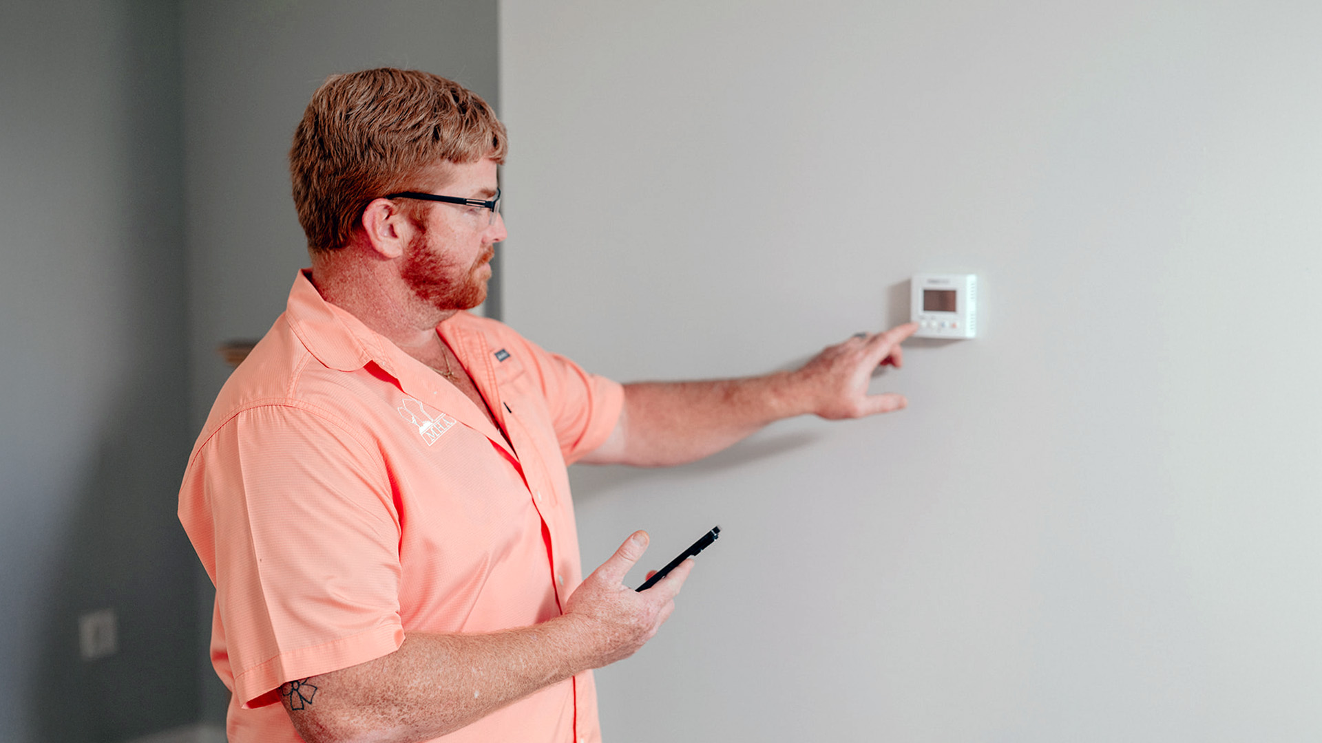 Man adjusting a thermostat on the wall while holding a smartphone.