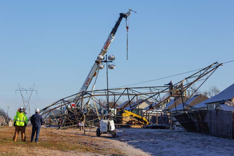 A crane is maneuvered into place to move a downed transmission tower.