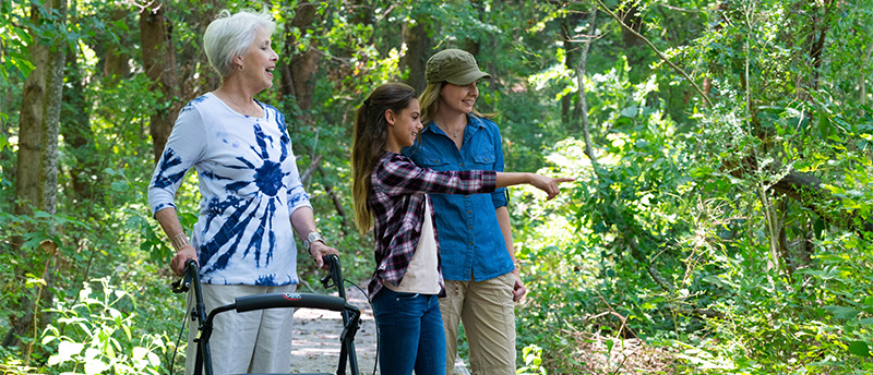Older woman using walker with woman and girl on accessible trail