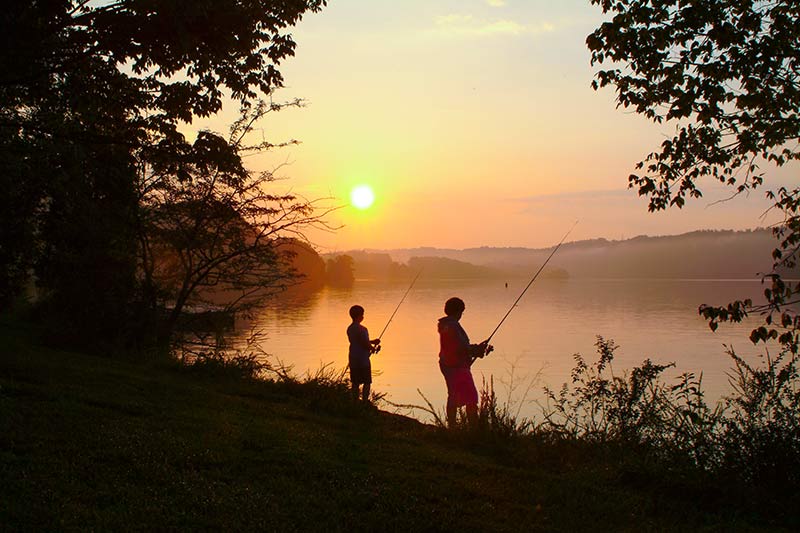 Two people fishing along a shoreline at sunset