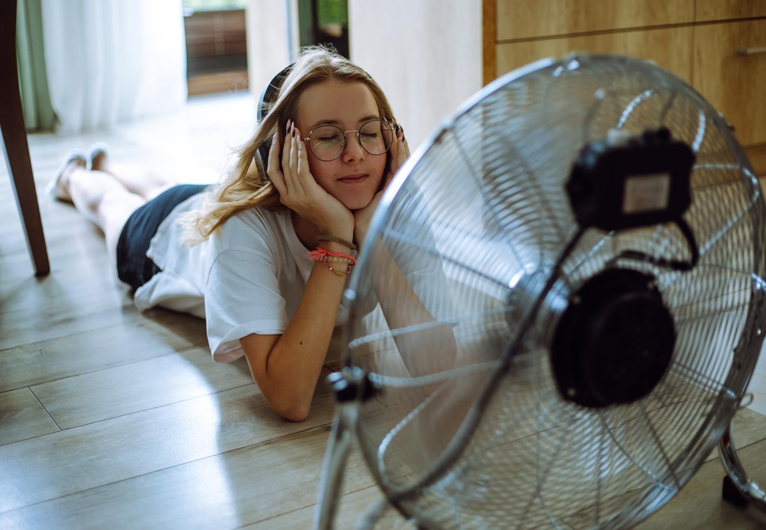 A teen girl creates on the floor, listening to music through wireless headphones in front of a cooling fan