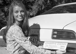 1970-hero-73186 woman placing "Conserve Energy" bumper sticker