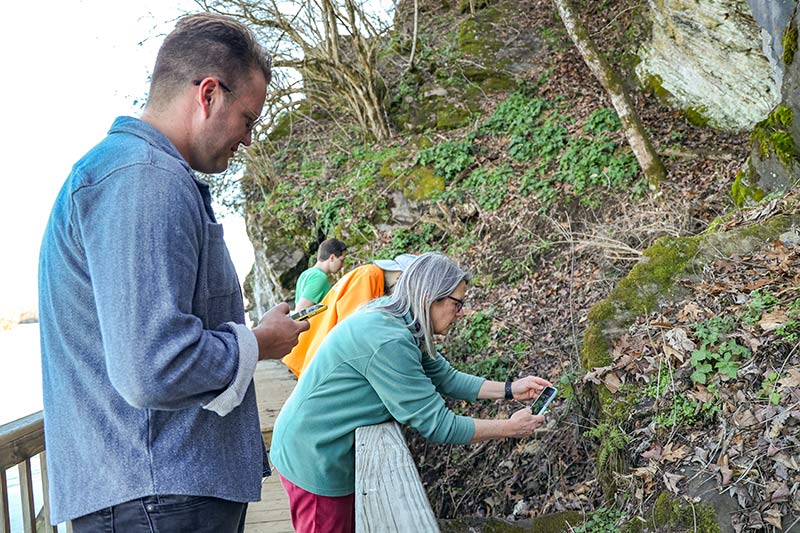 Nature program participants use smartphones to photograph plants near riverfront