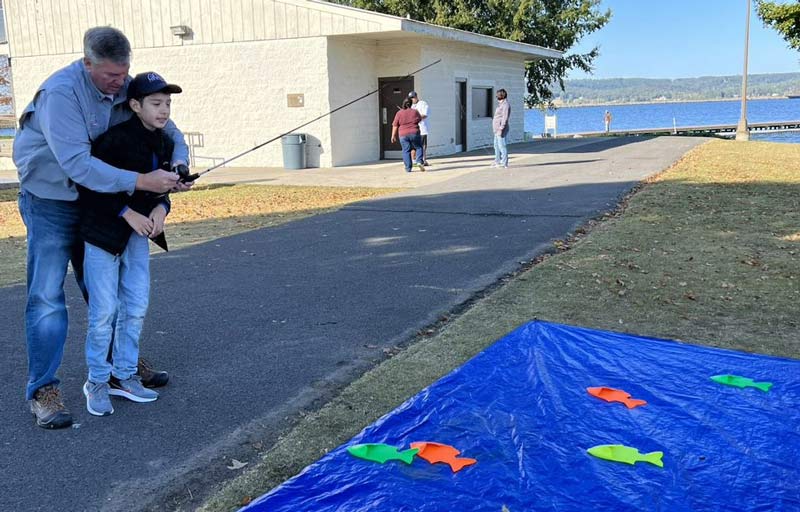 Eastern regional director Jeff Barnes helps participant Sebastian Aponte play a fishing game on land while waiting to board the boats.  