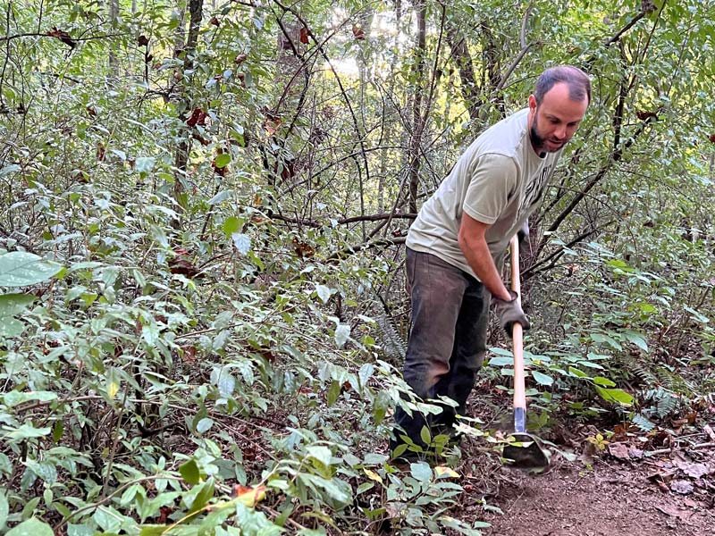 A man uses a digging implement to clear a trail edge at Loyston Point