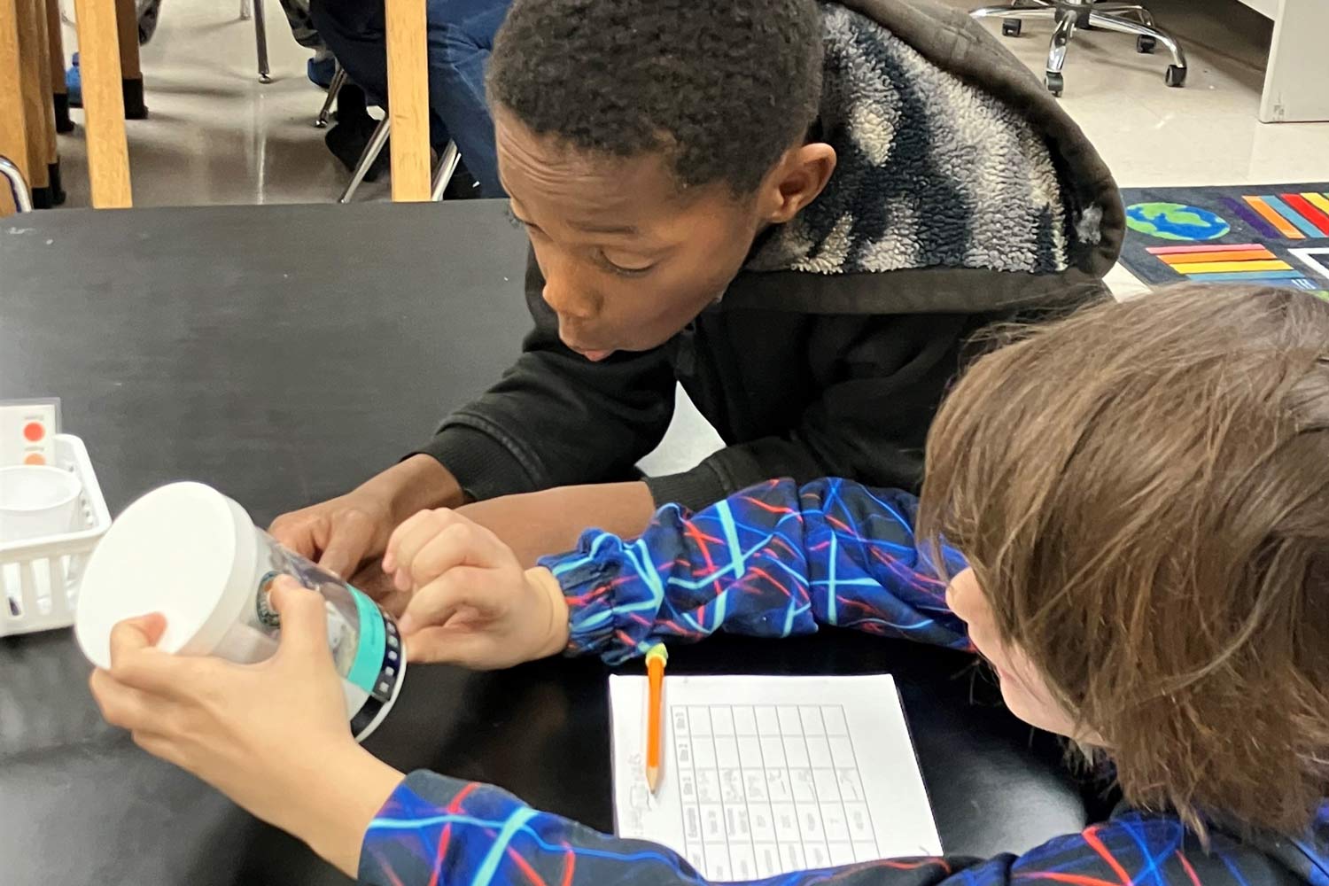 Two kids working together on a science project at a classroom table