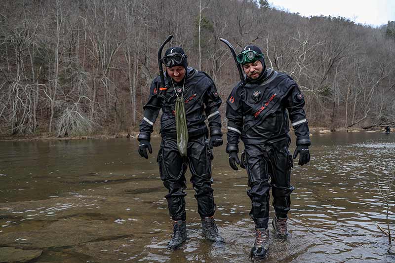 Biologists in cold diving gear walk through shallow water at Hiwassee River