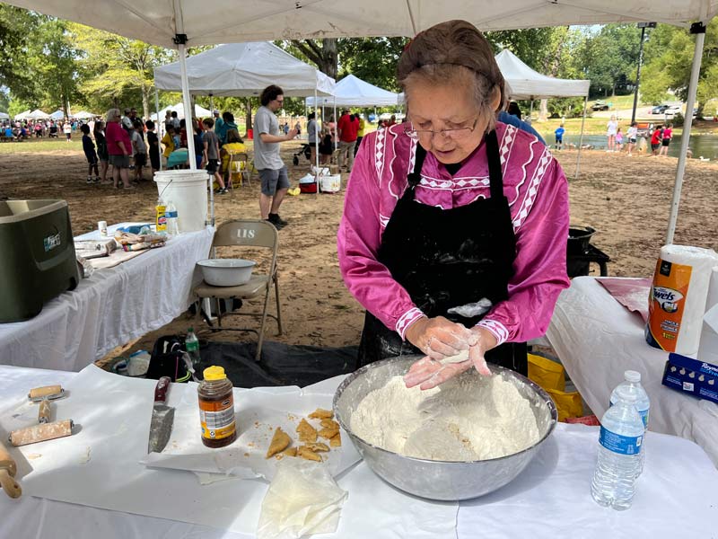 A woman in a bright pink shirt uses her hands to mix a thick dough in a bowl