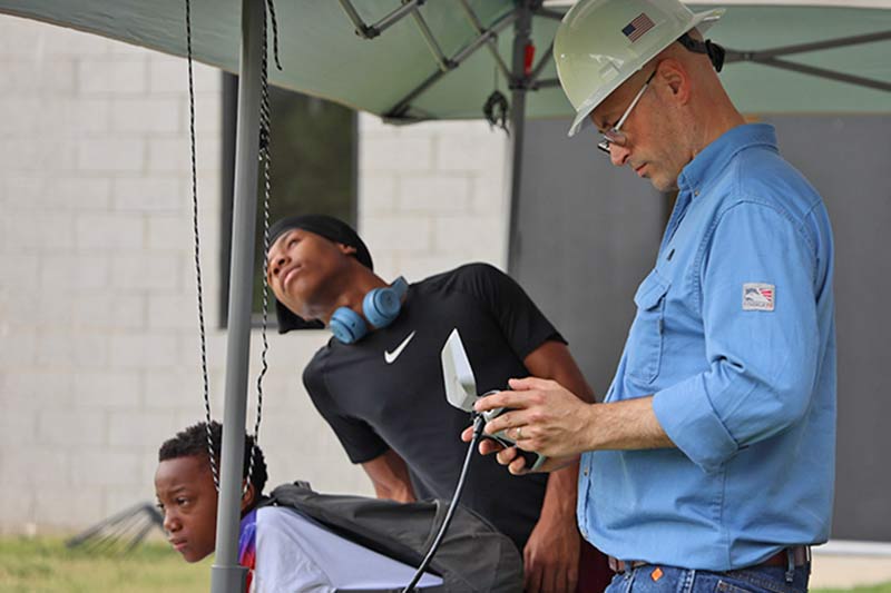 Taylor uses a handheld controller to fly a drone as students look on.