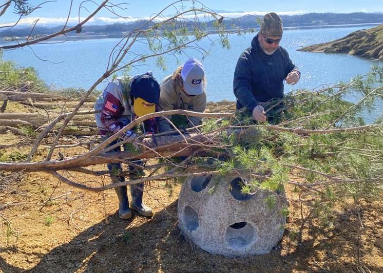 Three people working with branches by a lake.