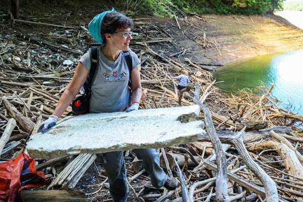 Person wearing gloves lifting a large piece of debris near a riverbank