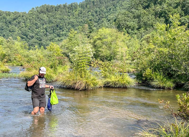 A TVA specialist carries his gear while walking in the river. 
