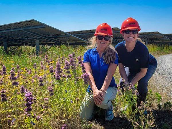 Two women in hard hat at a solar farm with wildflowers
