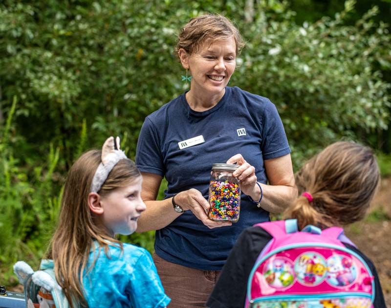 A TVA team member holds up a jar of colored beads as children look on