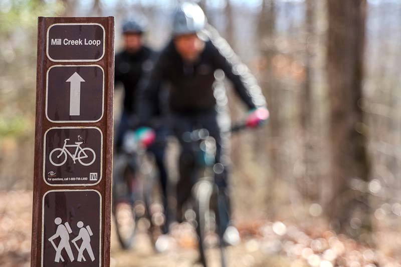 Two mountain bikers pass by a sign at Mill Creek Loop in the Loyston Point Trails system 