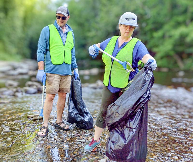 Volunteers place litter into a trash bag while cleaning a river in the Valley region