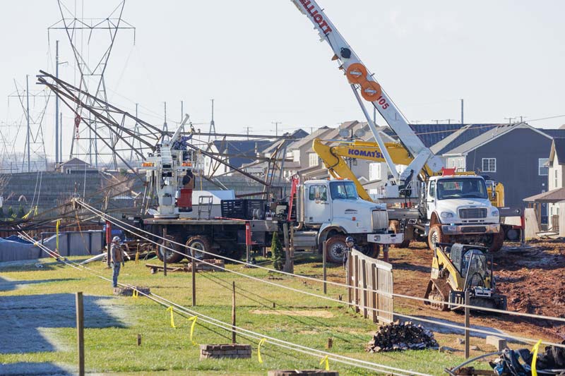 Work crews use cranes to lift transmission lines that were downed by storms
