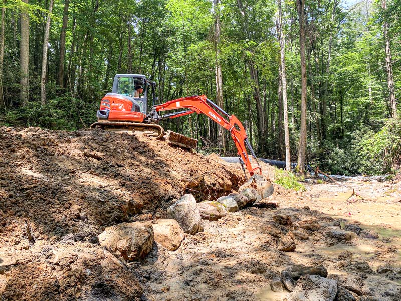 A worker uses an excavator to position boulders at the Wolf Creek bridge site